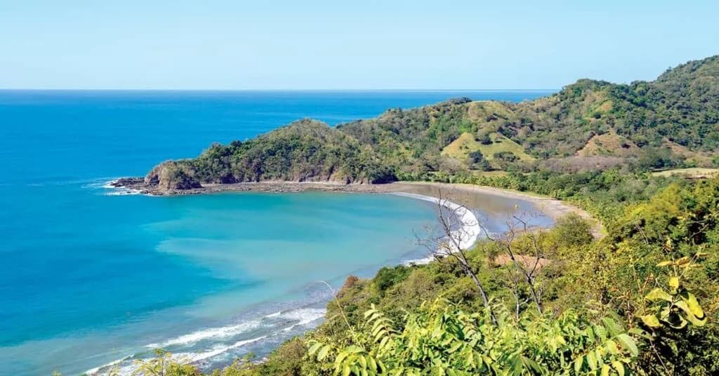 Bahía de aguas turquesa con playa en herradura y colinas verdes del Pacífico de Guanacaste